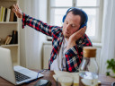 Young man with down syndrome sitting at a desk at home, using a laptop and listening to music with headphones