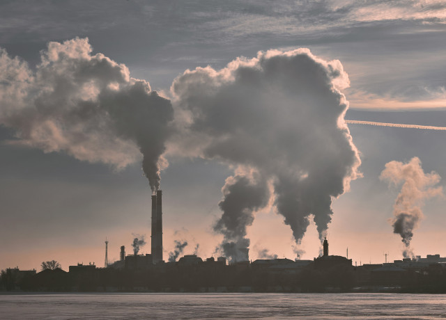 A large industrial complex with multiple smokestacks emitting thick clouds of smoke into the sky.